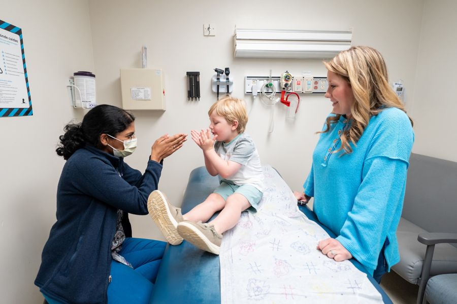 Female physician playing with male child patient while his mother watches