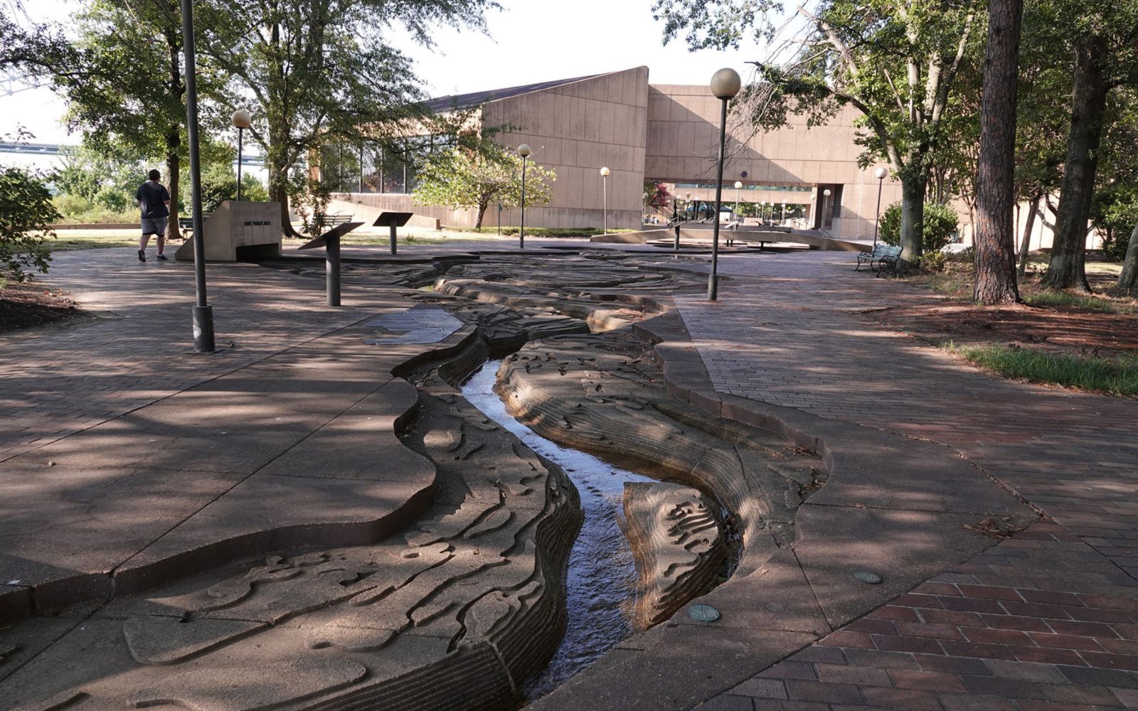 The Riverwalk, a scale model of the Mississippi River, under some trees facing a building.