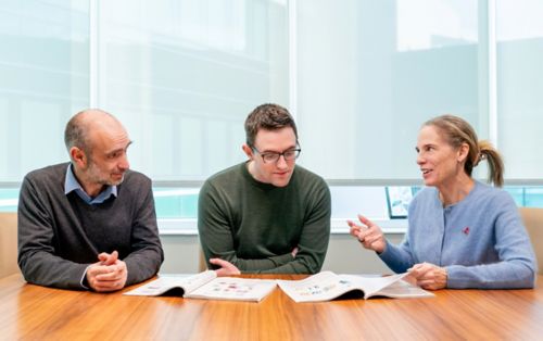 Two men and a woman seated at a table, talking about something in a magazine