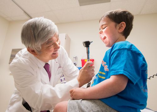 A male doctor examines a young male patients throat.