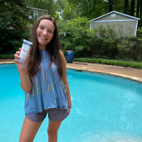 Woman standing outside holding sunscreen with pool in background