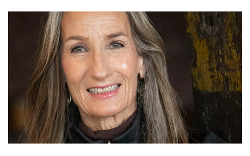 Smiling woman with long gray hair wearing hoop earrings and dark sweater, positive aging and wellness portrait