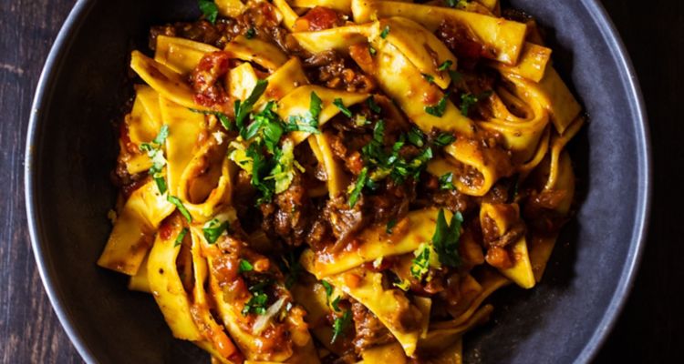 Pappardelle pasta dish with red sauce and green herbs