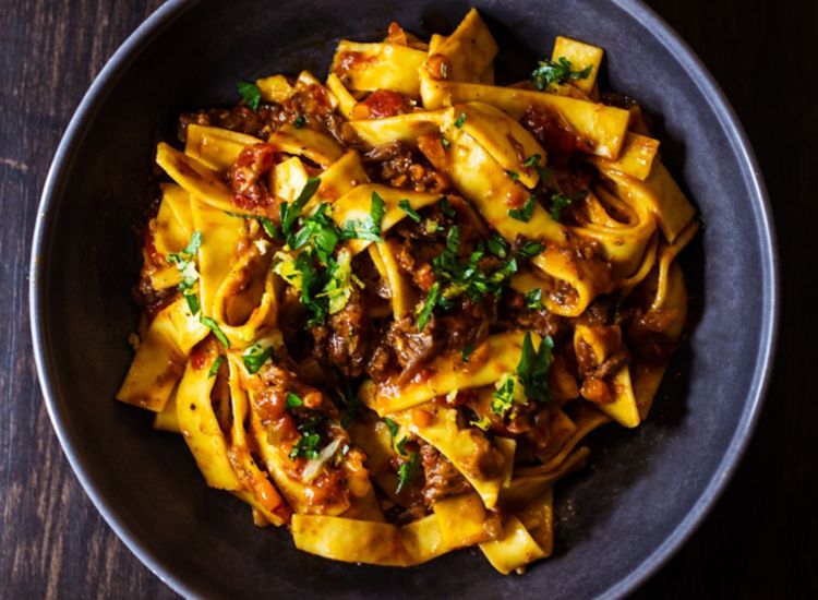 Pappardelle pasta dish with red sauce and green herbs