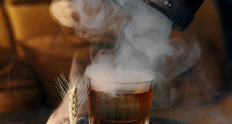 Glass of old fashion being unveiled from a barrel wih billowing smoke