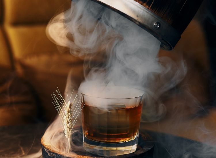 Glass of old fashion being unveiled from a barrel wih billowing smoke