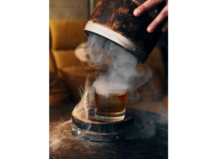 Glass of old fashion being unveiled from a barrel wih billowing smoke