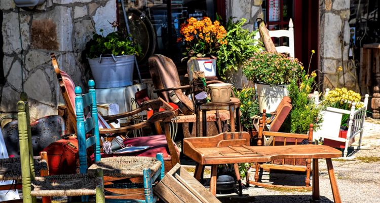 Outside of a store with antique furniture and potted flowers.
