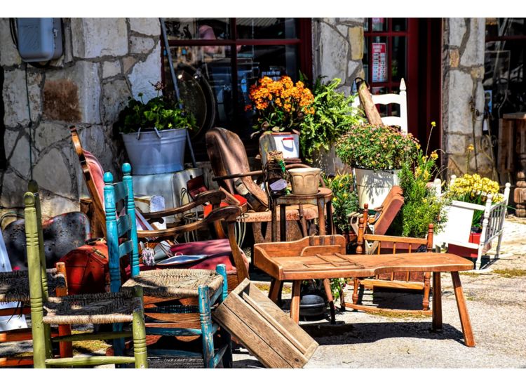 Outside of a store with antique furniture and potted flowers.