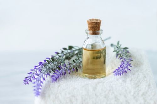 Front view of lavender in oil and lavender flowers on a white towel on marble background.