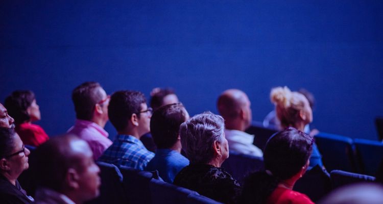 Audience watching a performance in a blue room.