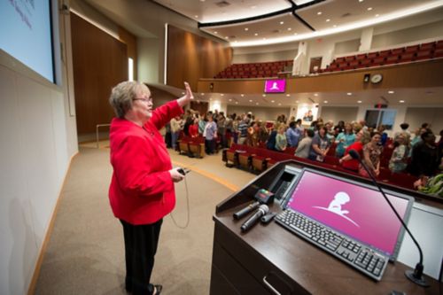 Photo of woman in red jacket speaking to large audience