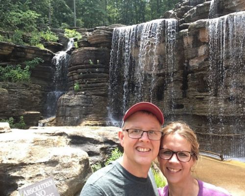 Billy and his wife take a photo in front of a waterfall