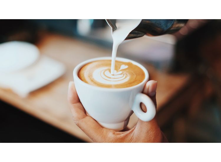 Hand holding white cup of coffee and pouring milk into a design