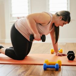 Woman on yoga mat lifting dumbbell