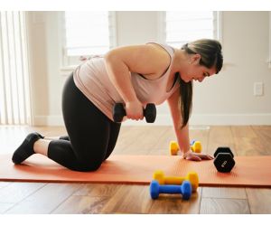 Woman on yoga mat lifting dumbbell