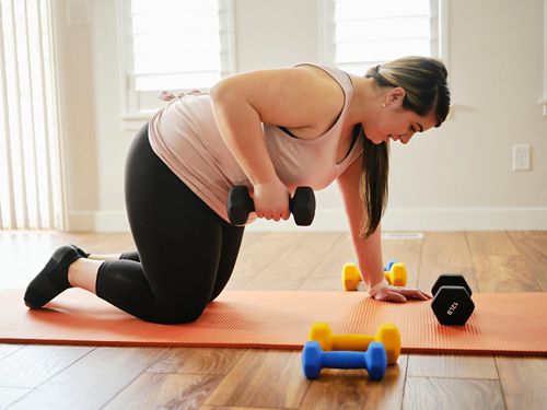 Woman on yoga mat lifting dumbbell 