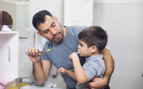 Father helps son brush teeth