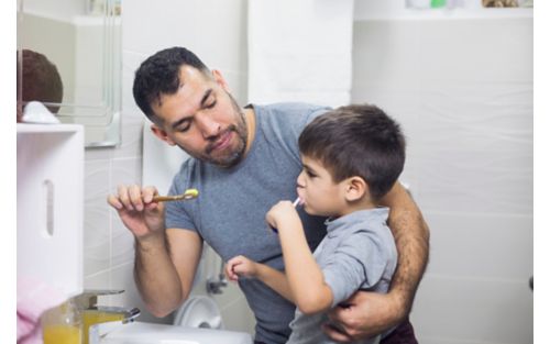 Father helps son brush teeth