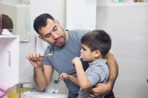 Father teaching son how to brush his teeth correctly. 