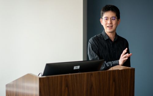 Imnage of Chi-:Lun Chang, in black shirt, standing at podium