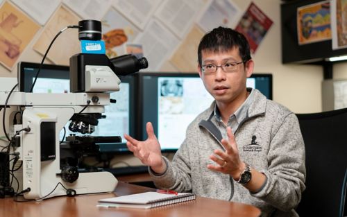 Photo of Jason Chiang sitting at a desk with a microscope and computer screens