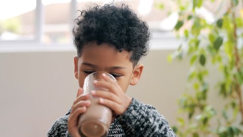 Fotografía de un niño bebiendo una malteada de chocolate en casa.