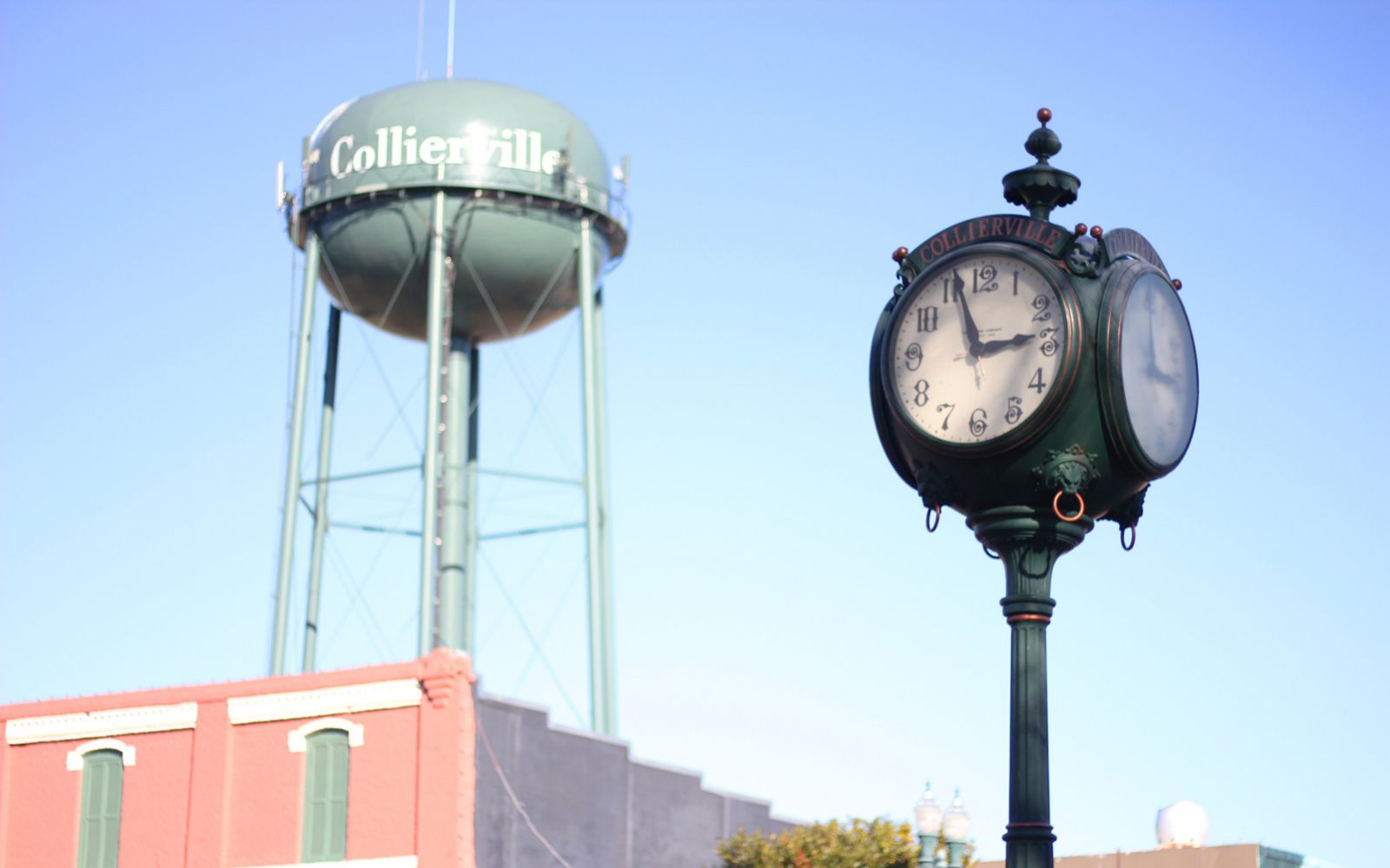 Green Collierville water tower with a clock on a pole in the foreground.