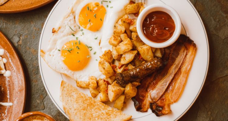 White breakfast plate with eggs, toast, bacon sausage, hashbrowns and ketchup