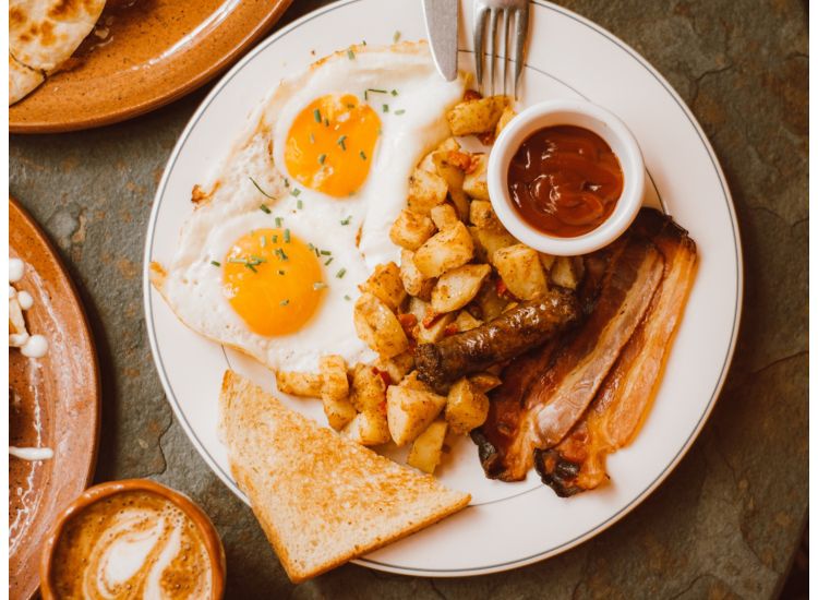 White breakfast plate with eggs, toast, bacon sausage, hashbrowns and ketchup