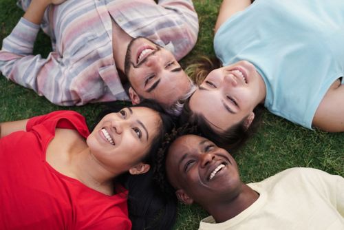 Four teenagers in circle smiling while laying down outdoors