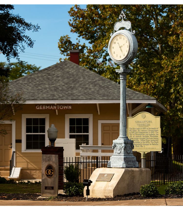 A small yellow building with a Germantown sign with a clock on a pole in front.