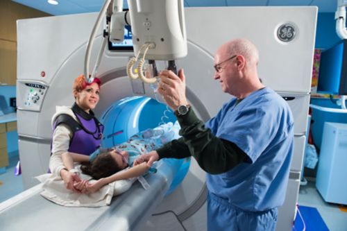 CT technologist administers contrast to a pediatric cancer patient with her mom nearby.