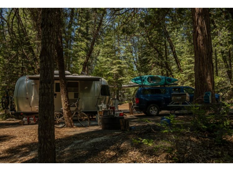   Pick up truck towing an airstream trailer with camping gear in the woods.