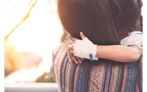 Child with bandaged hand and IV hugs mothe.