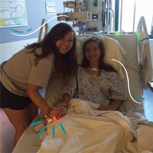 Emma laying in a hospital bed with a friend standing nearby.