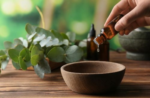 Femme versant de l'huile essentielle d'eucalyptus dans un bol sur une table en bois