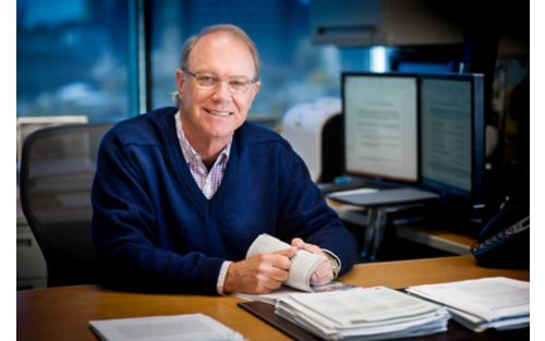 Image of man in blue sweater at desk. 