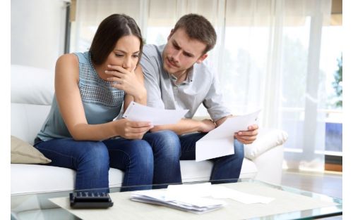 man and woman sitting on a couch looking concerned at some papers