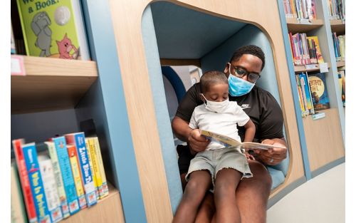 Father holds young son while reading a book together.