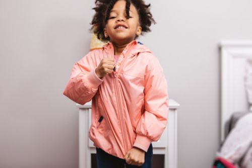 Child smiles while zipping up jacket.