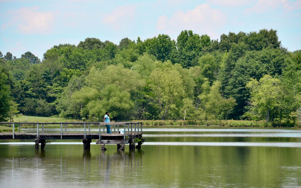 Man relaxes on a pier in a lake with fishing rods resting on the railing.