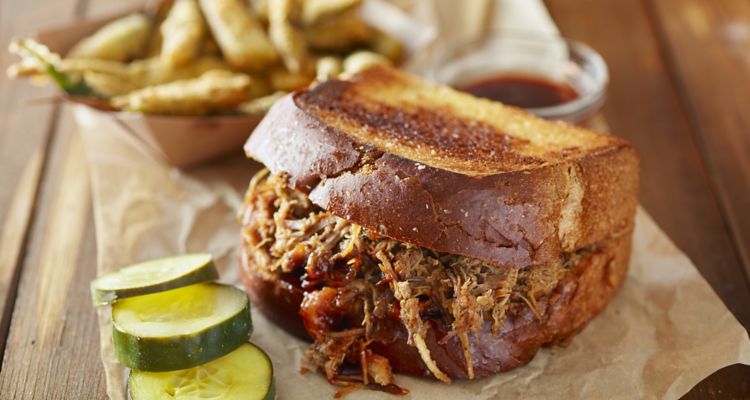 Pulled pork sandwich with fries and pickles on a wooden table