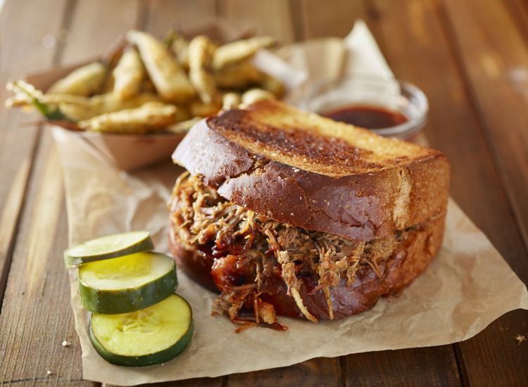 Pulled pork sandwich with fries and pickles on a wooden table
