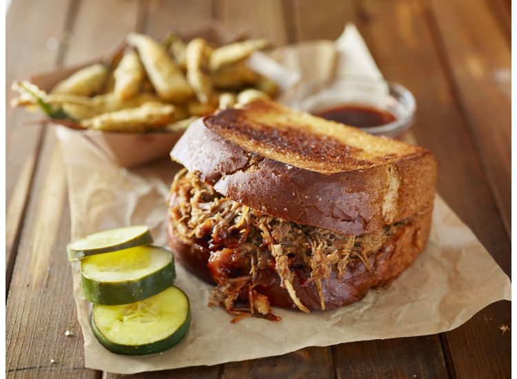 Pulled pork sandwich with fries and pickles on a wooden table