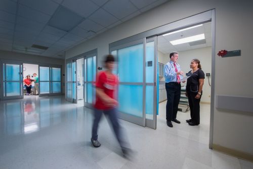 Photo shows two people talking inside doorway as young person passes by