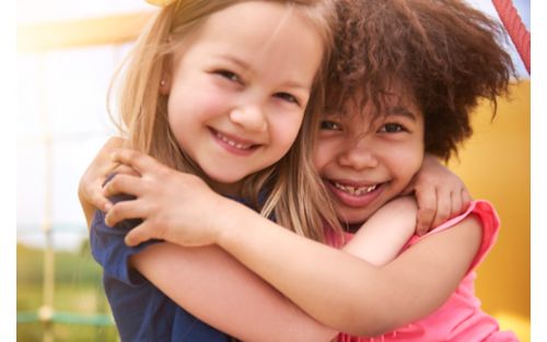 Two young girls smiling and hugging outdoors