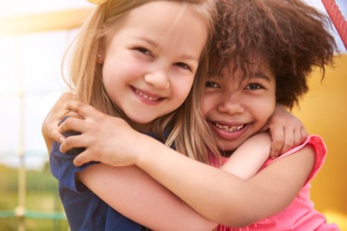 Two young girls smiling and hugging outdoors