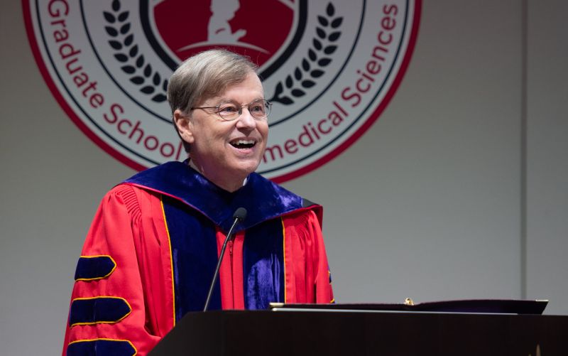 Man in red gown behind podium.