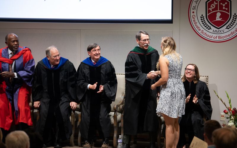 Woman in dress shaking hands with man in academic regalia